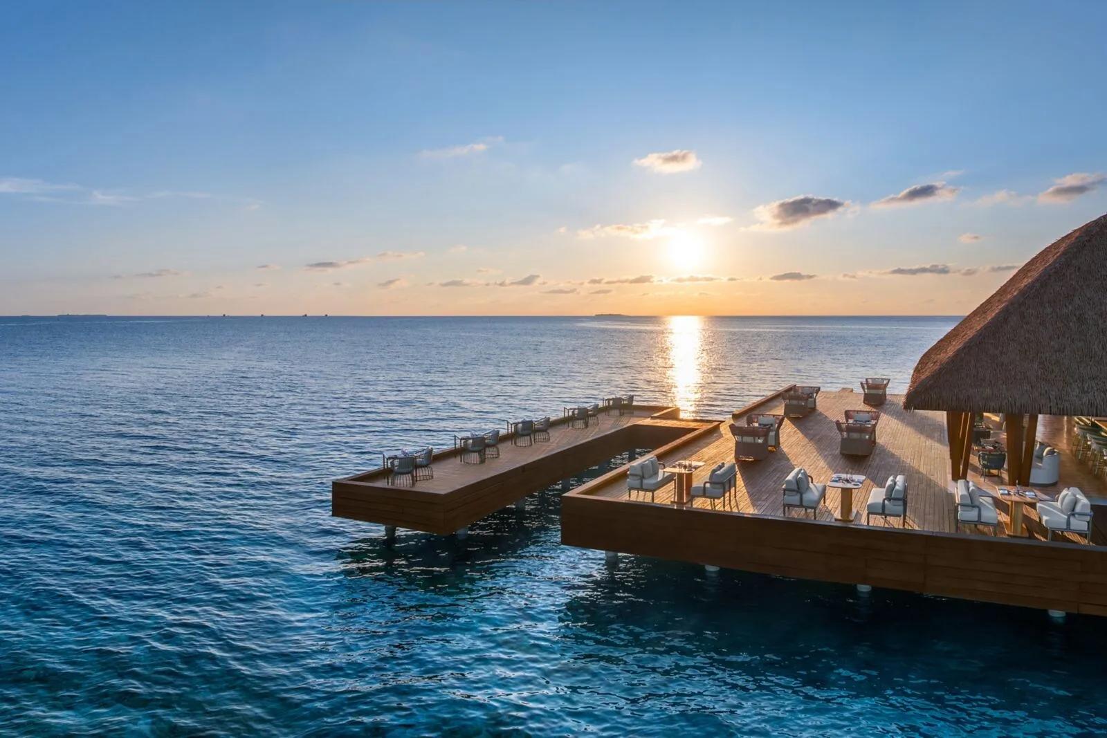 FISH, W Maldives' overwater seafood restaurant, its open-air deck set for dinner as the sky turns orange at sunset