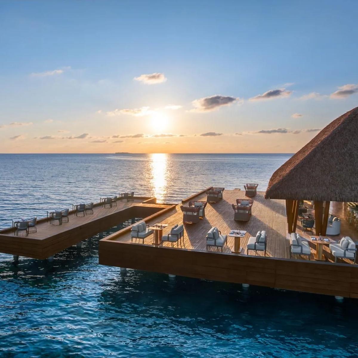 FISH, W Maldives' overwater seafood restaurant, its open-air deck set for dinner as the sky turns orange at sunset
