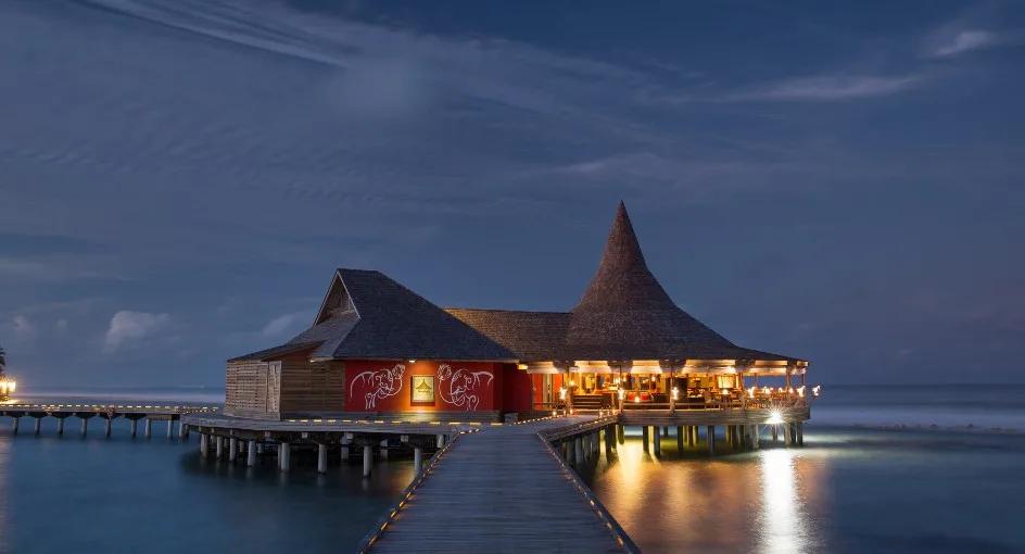 Baan Huraa, the resort's Thai restaurant built as a teak house on stilts over the lagoon, lit at evening