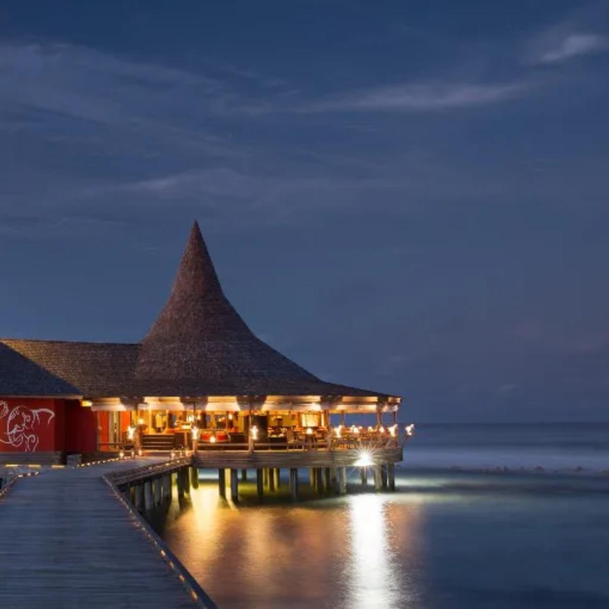 Baan Huraa, the resort's Thai restaurant built as a teak house on stilts over the lagoon, lit at evening