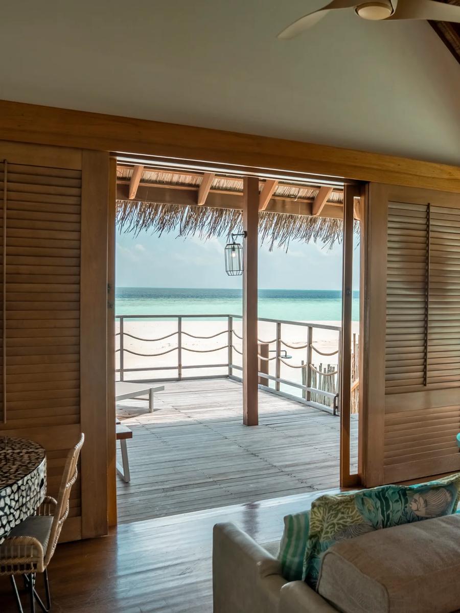 Senior Water Villa living area with a long sofa facing floor-to-ceiling windows and a rope-railed deck over the lagoon