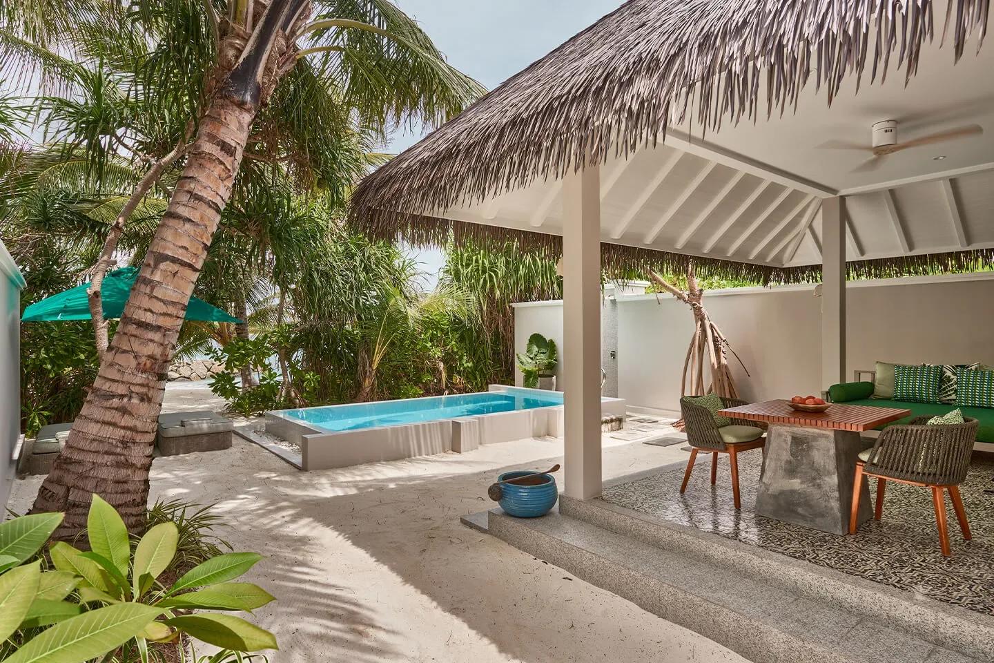 A Private Pool Villa's plunge pool and thatched-roof outdoor dining pavilion, framed by a leaning palm and tropical garden planting