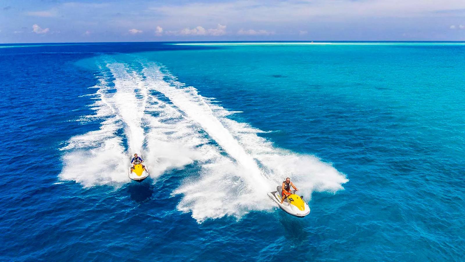 Two jet skis carving parallel wakes across clear lagoon water