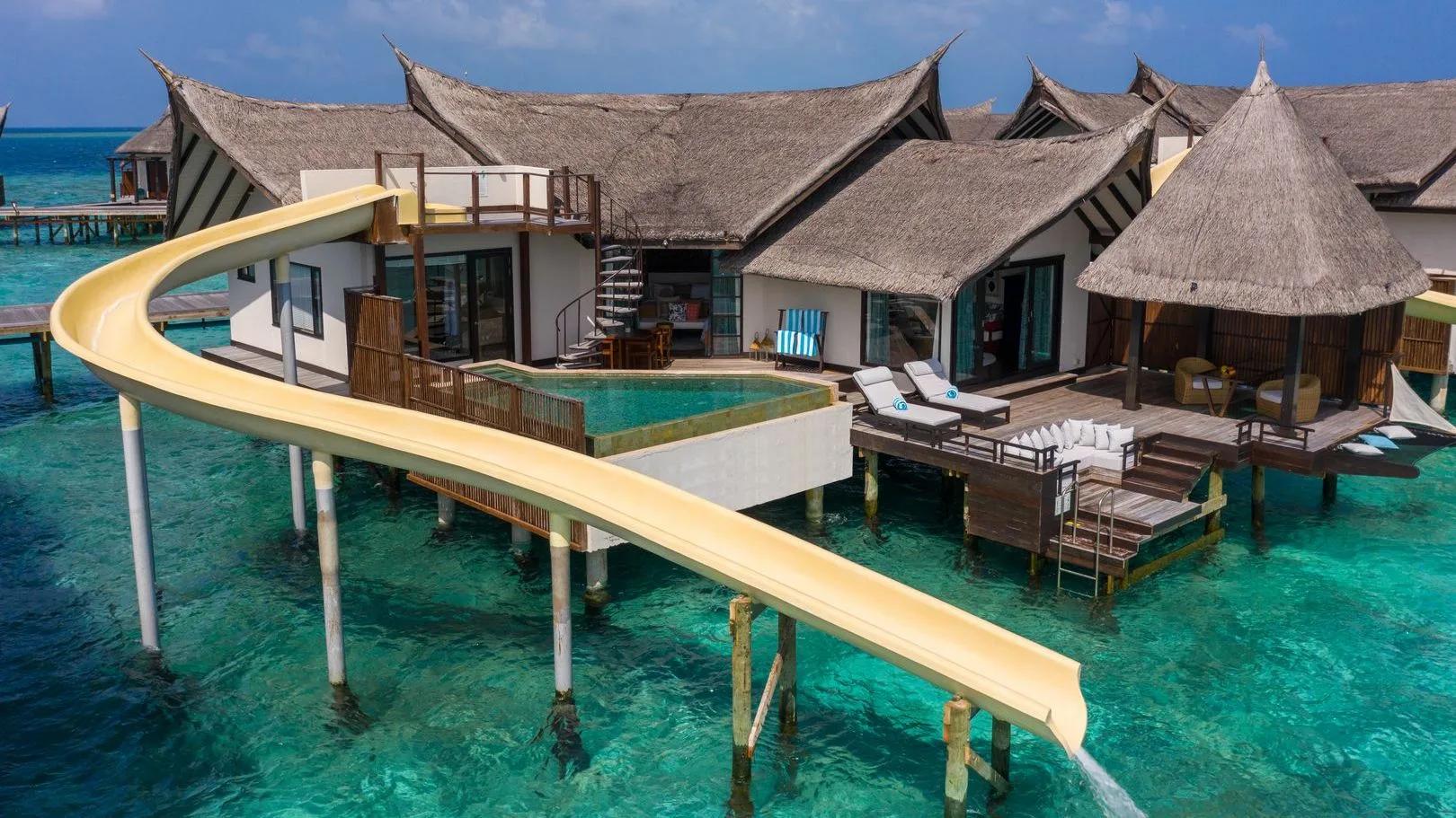 An Ocean Pool Suite with Slide, its yellow water slide curving from the upper deck into the lagoon beside the villa's private pool