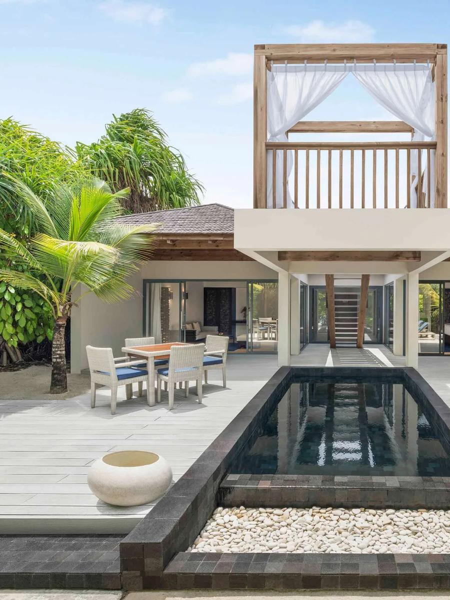 Exterior of a beach pool villa with a private pool, dining table, hanging egg chair and an elevated daybed loft among palm trees