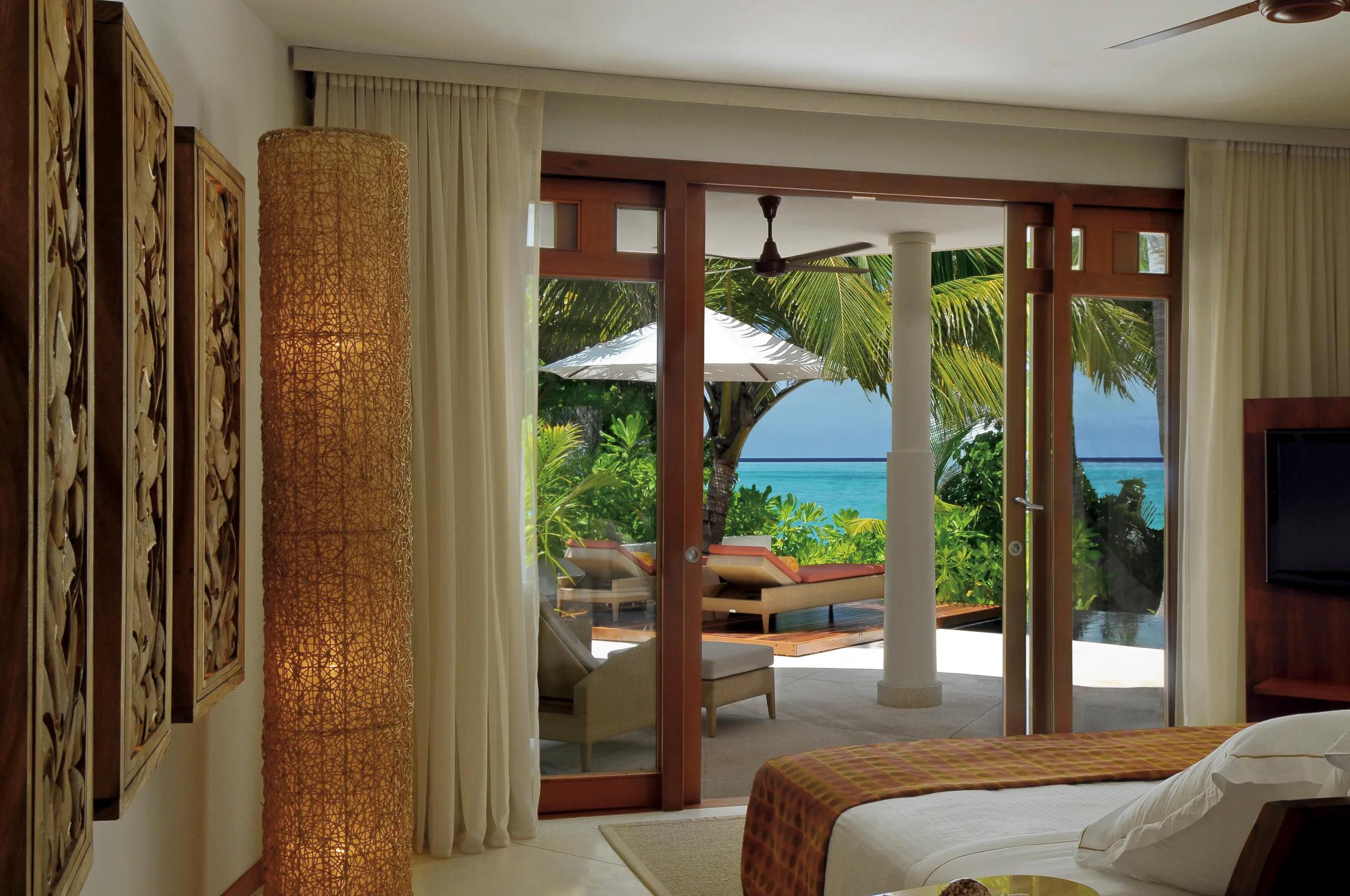 The bedroom of a Double Storey Beach Villa, with glass doors open to a furnished terrace, sun loungers, and a glimpse of the plunge pool beyond