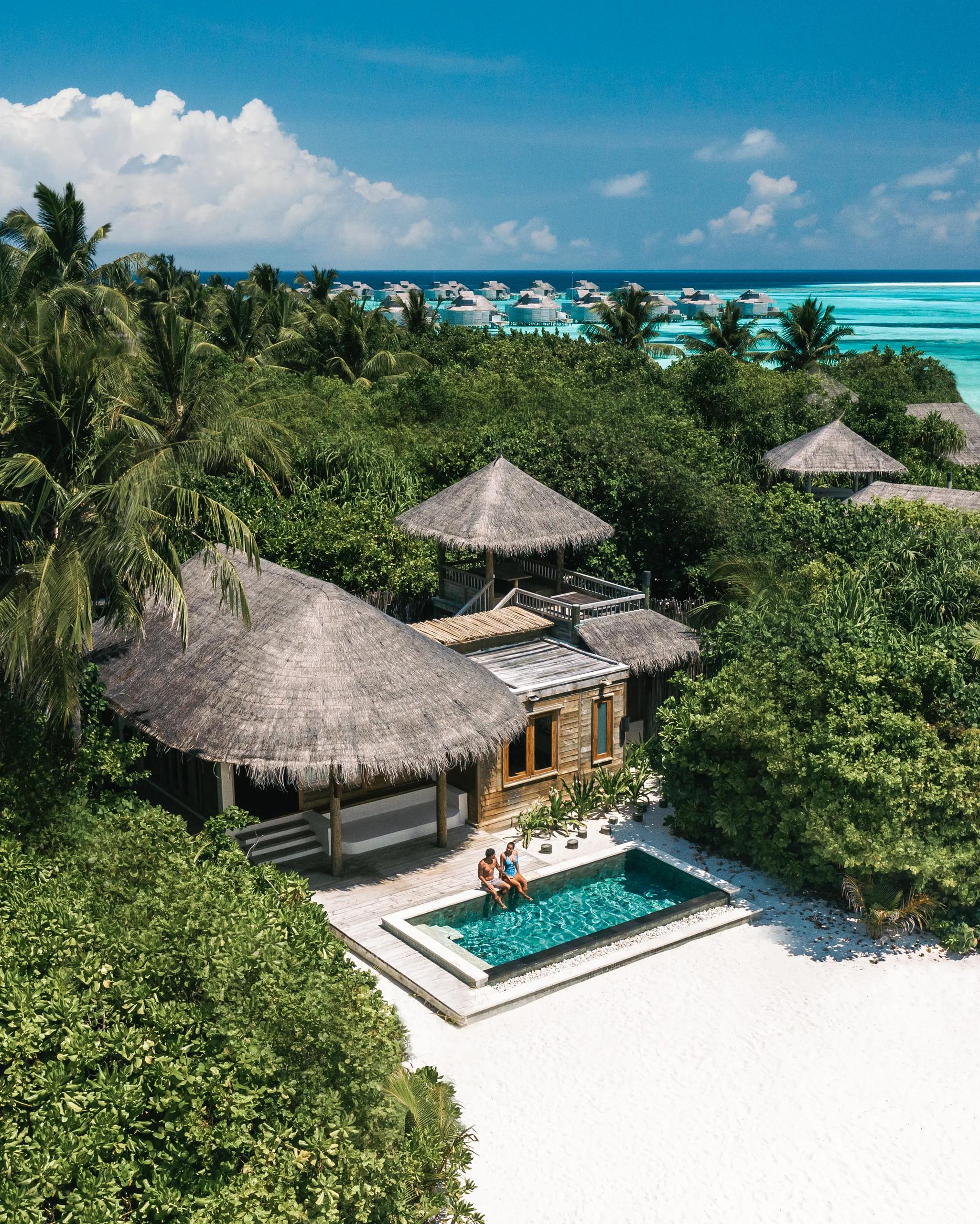 A view over jungle canopy toward a row of distant overwater villas and the open sea