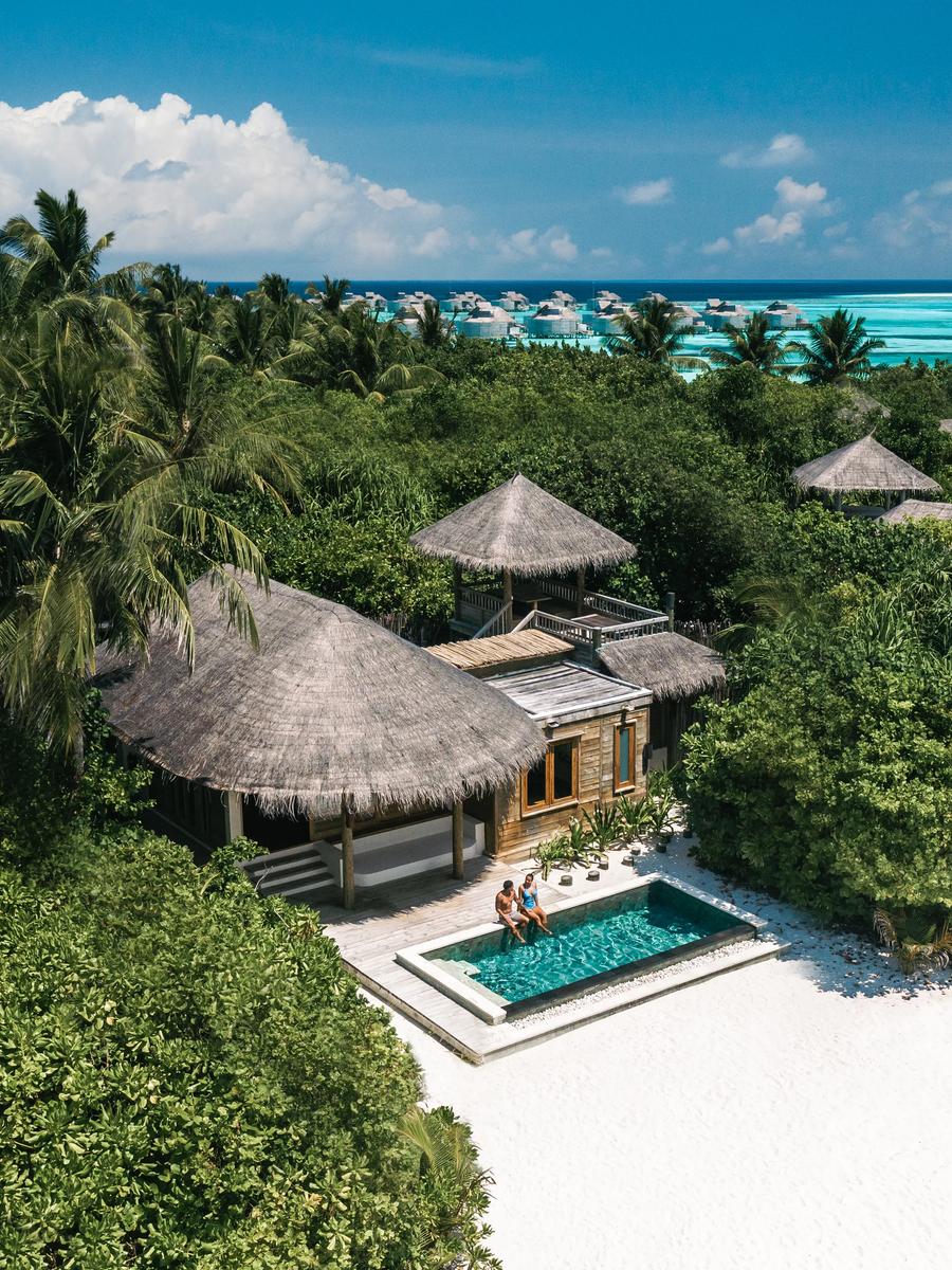 A view over jungle canopy toward a row of distant overwater villas and the open sea