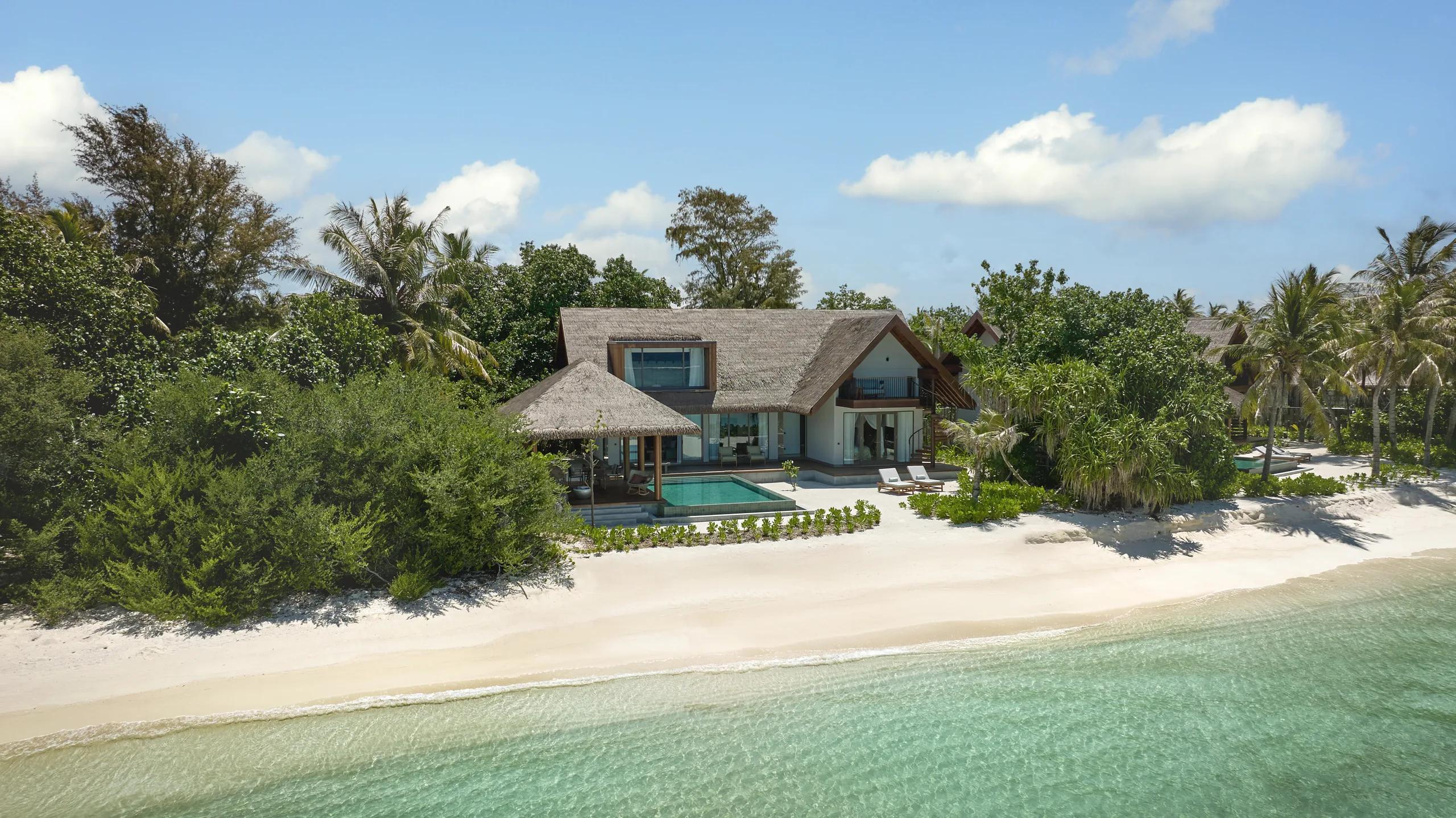 A Beach Retreat with Pool seen from the beach, its thatched roofline set behind a line of trees, with a private pool in the foreground.