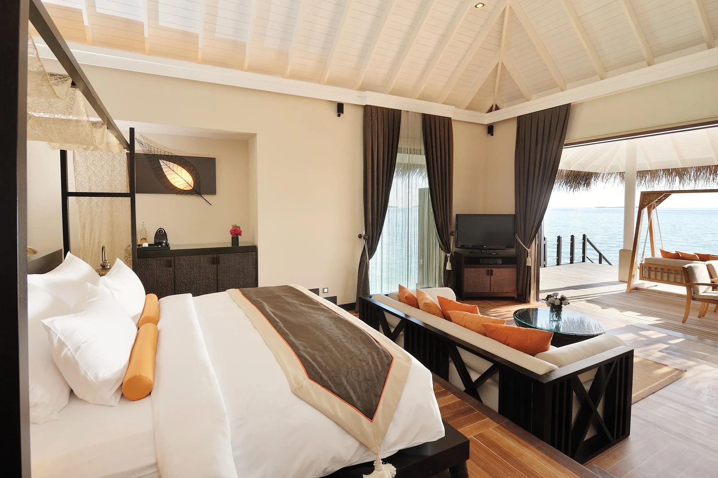 A Sunset Lagoon Suite bedroom opening onto an overwater deck with a swing seat above the shallows