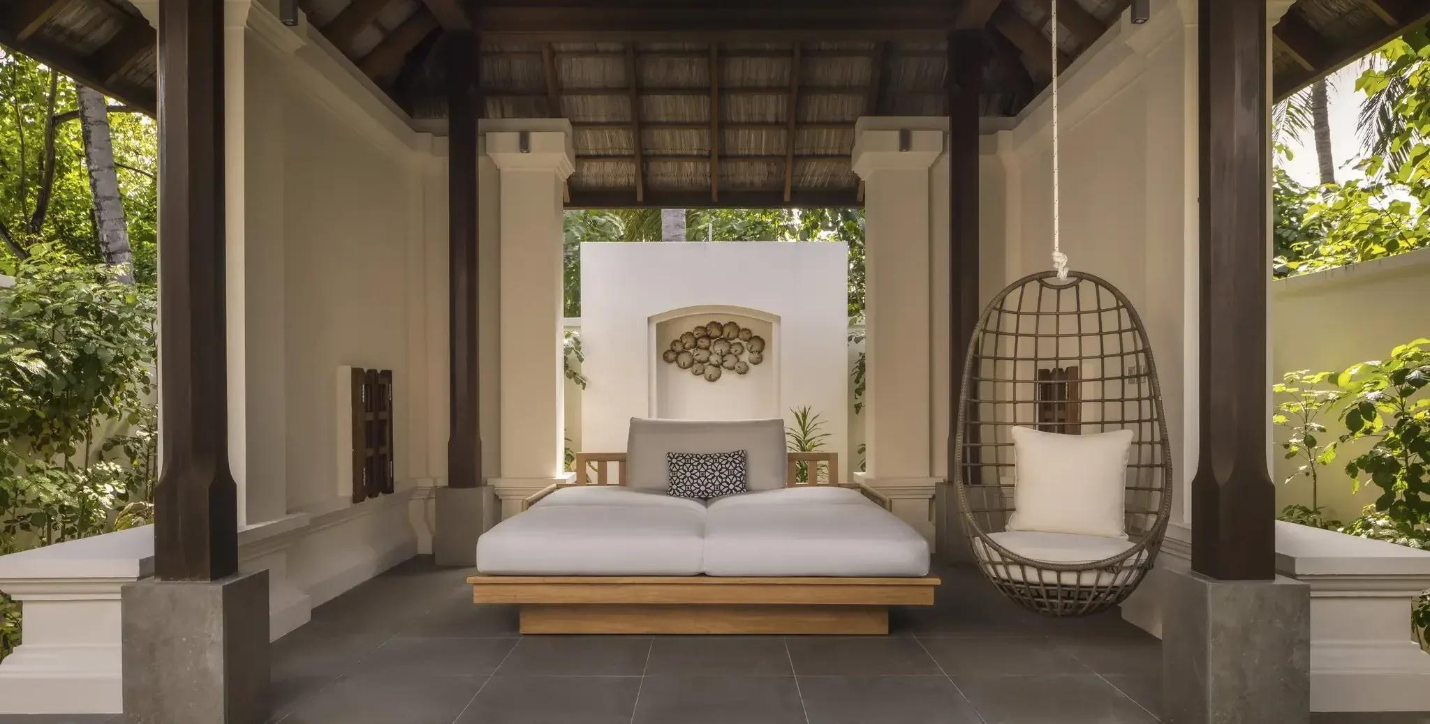 An open-air daybed and hanging chair on the garden terrace of a Deluxe Beach Villa with Pool