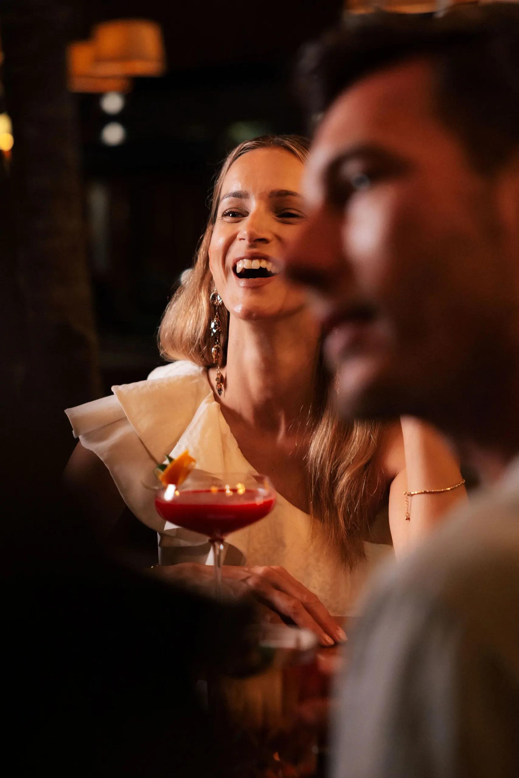 A woman laughs over a red cocktail at Cru's bar in the evening light