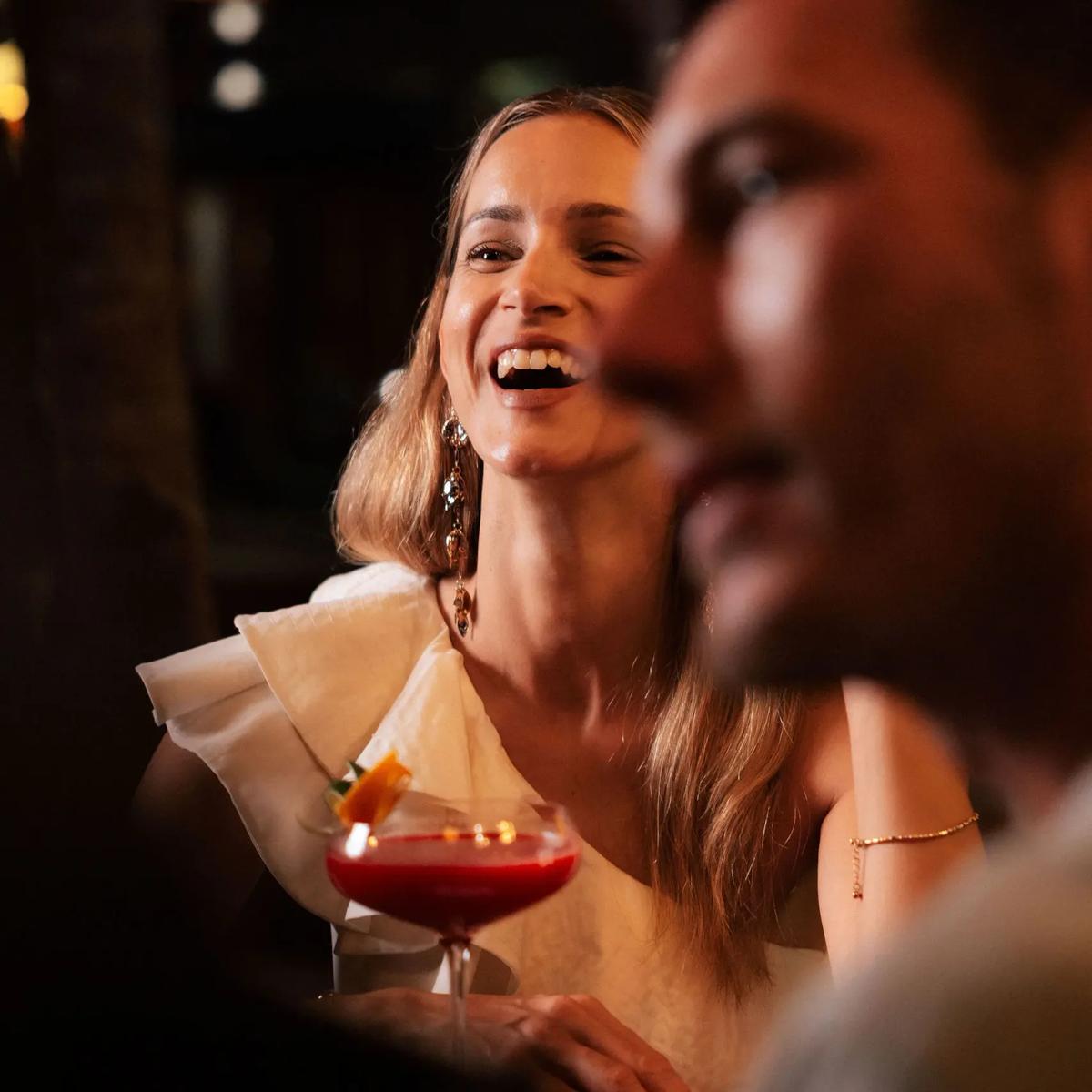 A woman laughs over a red cocktail at Cru's bar in the evening light