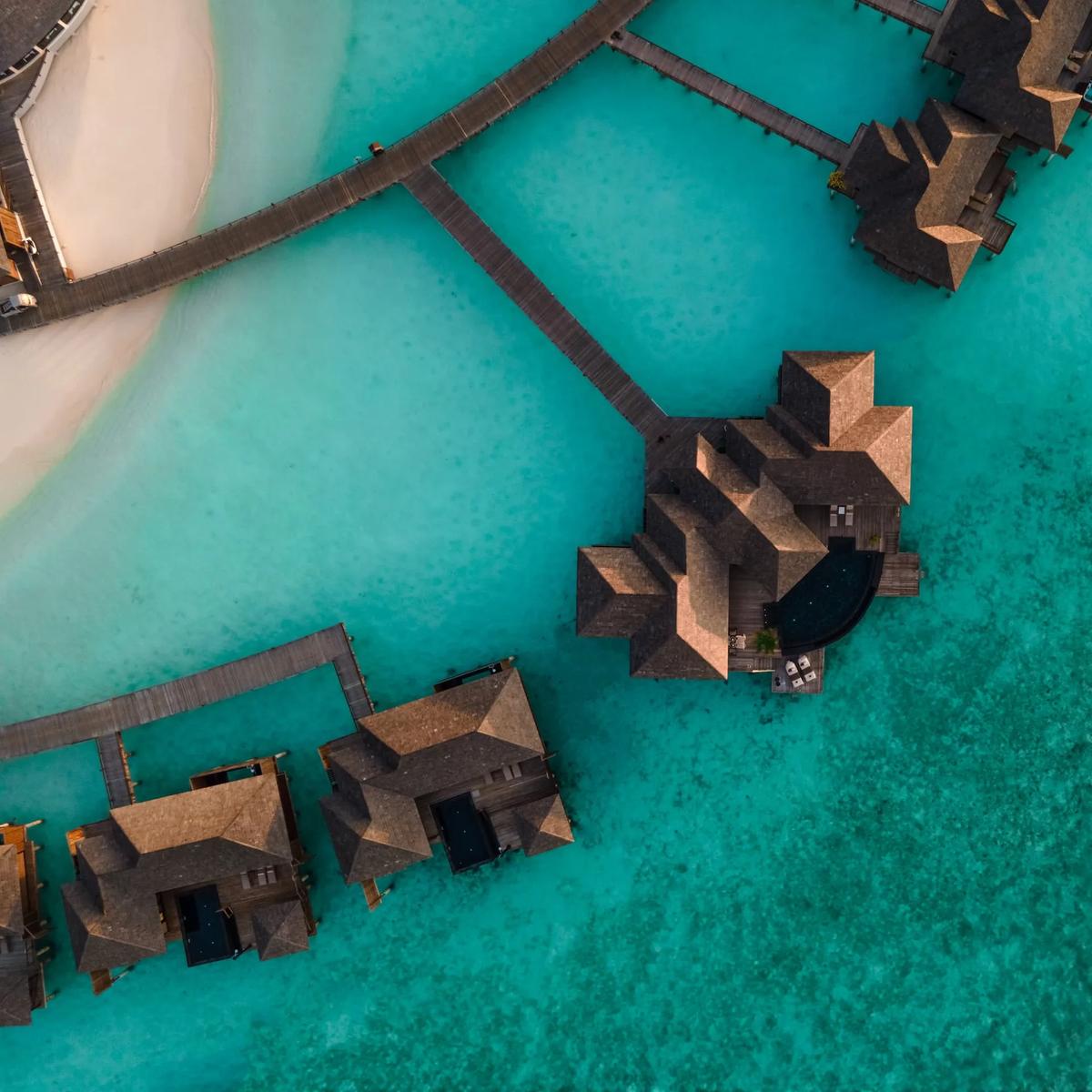 Aerial view of Sun Siyam Iru Fushi's overwater villas and private pools set over the turquoise Noonu Atoll lagoon