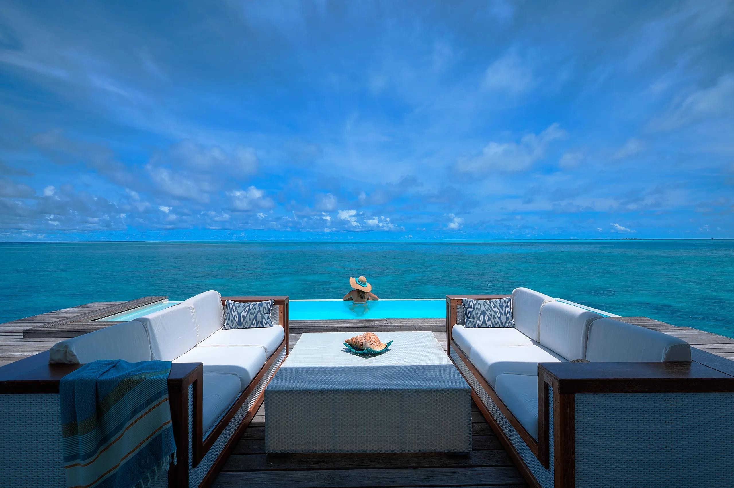 A guest wading into the infinity-edge pool of a Two Bedroom Pool Water Villa, reef water stretching to the horizon