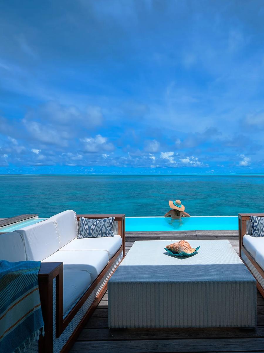 A guest wading into the infinity-edge pool of a Two Bedroom Pool Water Villa, reef water stretching to the horizon