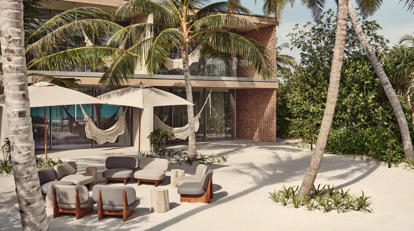 The brick and timber exterior of a Fari Studio at Patina Maldives, hammocks strung between its palms