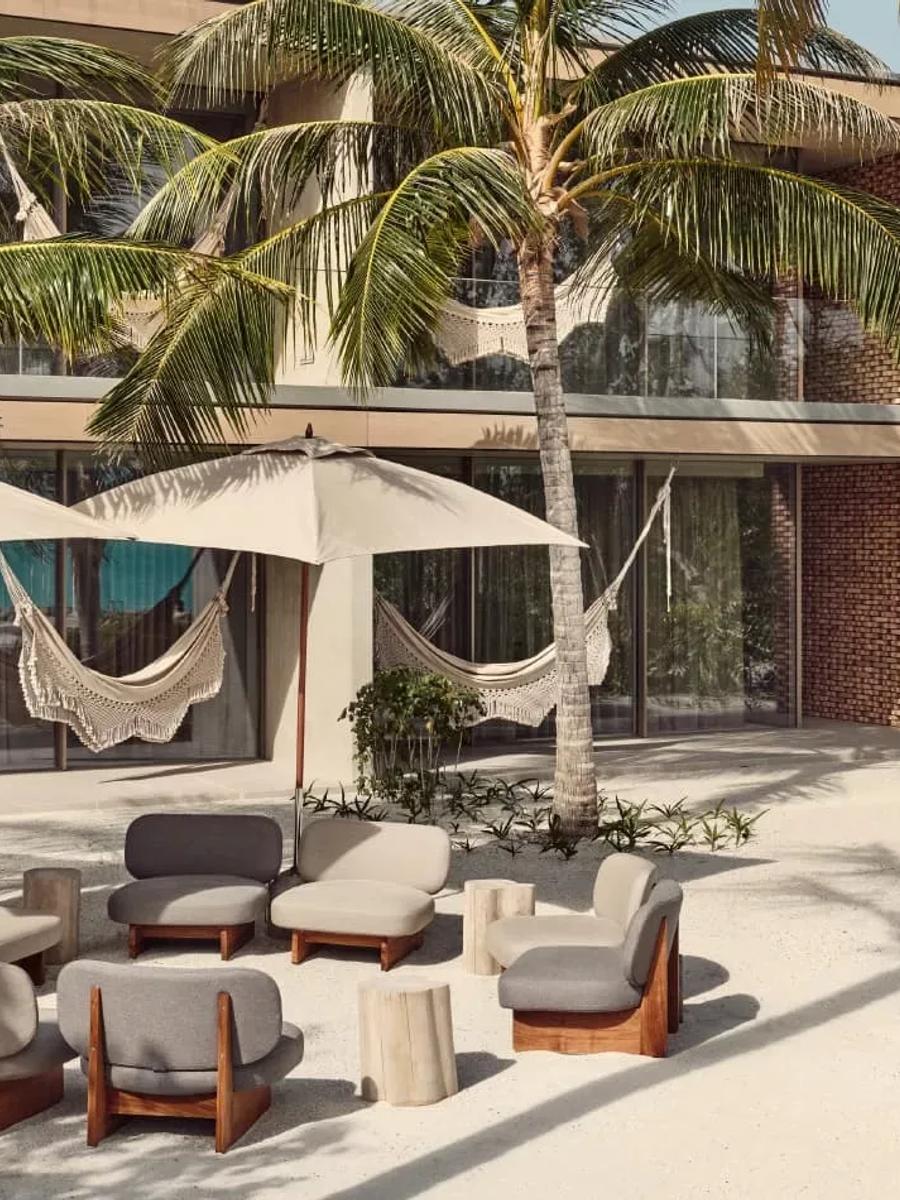 The brick and timber exterior of a Fari Studio at Patina Maldives, hammocks strung between its palms