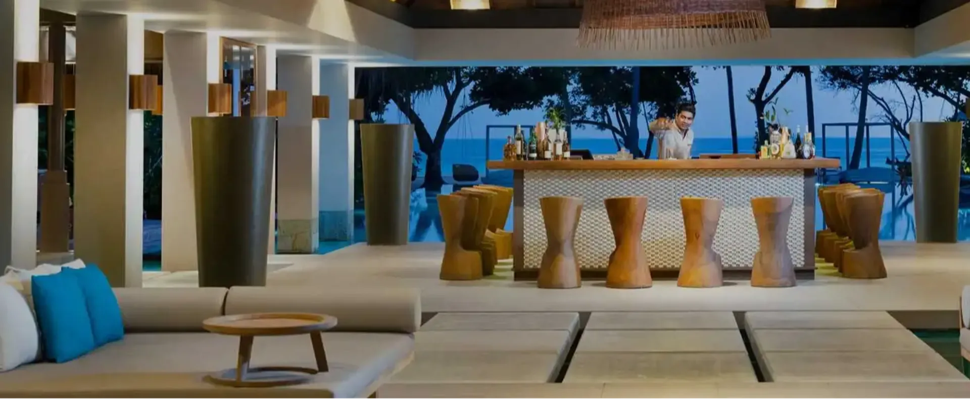 Cabana's poolside bar at dusk, a bartender pouring drinks with the pool and beach visible behind