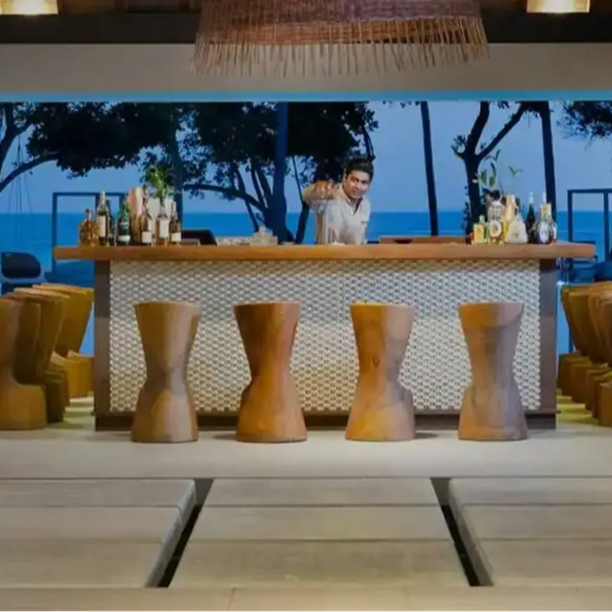 Cabana's poolside bar at dusk, a bartender pouring drinks with the pool and beach visible behind
