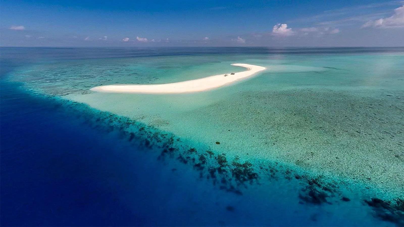 Dream Island, a curved white sandbank off Hurawalhi used for wedding and vow-renewal ceremonies, the reef dropping into deep blue water beyond