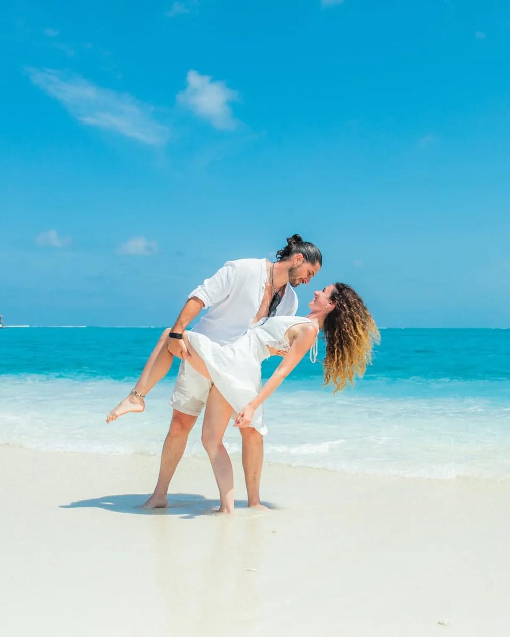 A honeymoon couple in the calm shallows of a Maldivian lagoon at golden hour