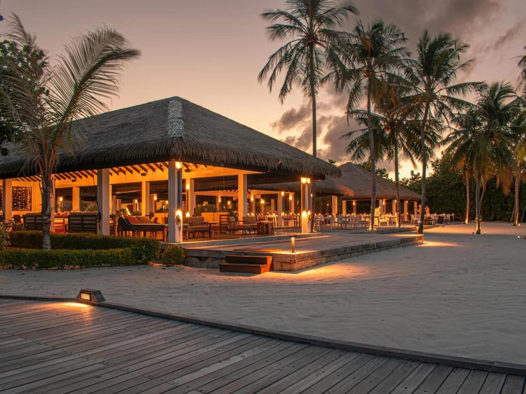 Palms Restaurant's thatched beachfront pavilion at Noku Maldives, lit for dinner service at dusk