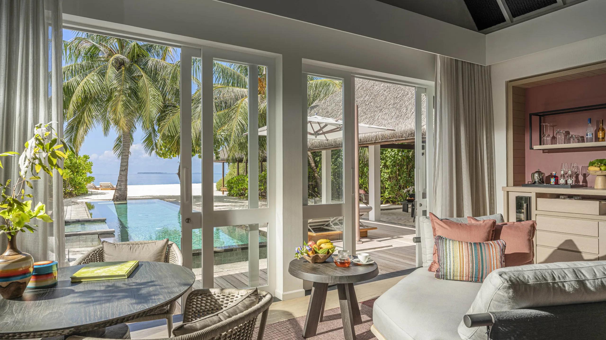 A Beach Villa's living area opening onto its private pool, which runs almost to the beach beneath a shading palm tree