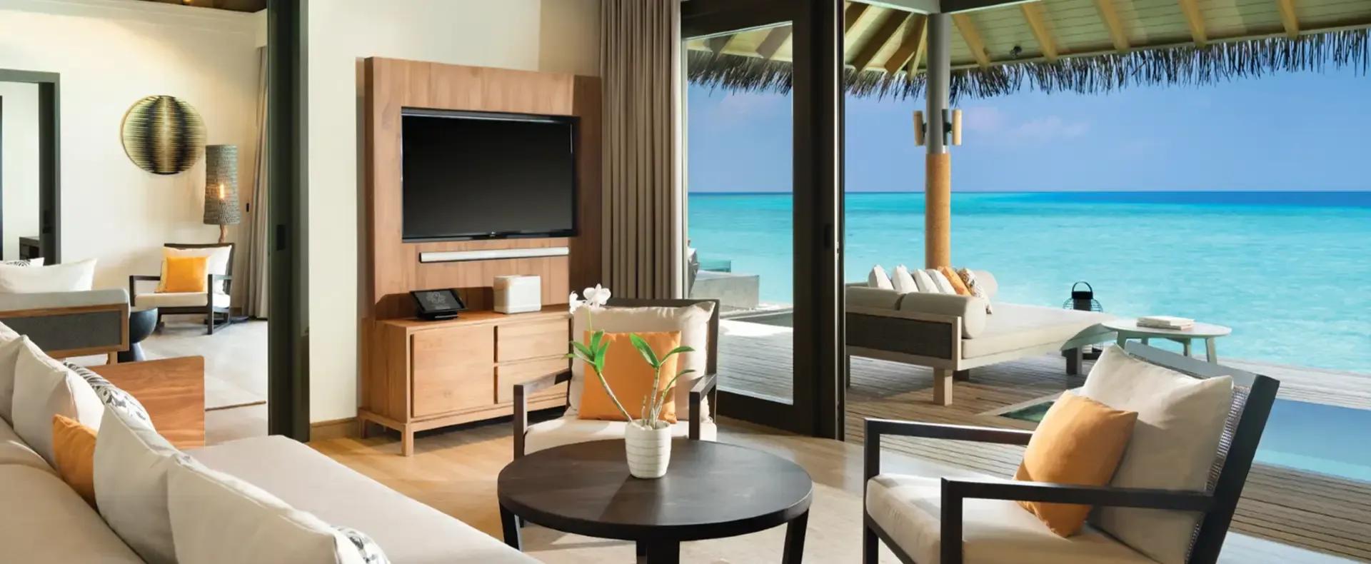 Living room of a One Bedroom Over Water Pool Residence, sofa and TV console beside glass doors opening onto the lagoon