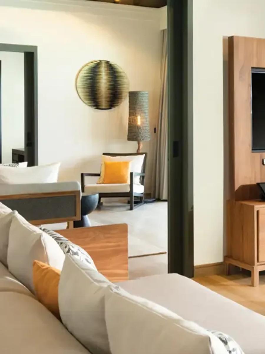 Living room of a One Bedroom Over Water Pool Residence, sofa and TV console beside glass doors opening onto the lagoon