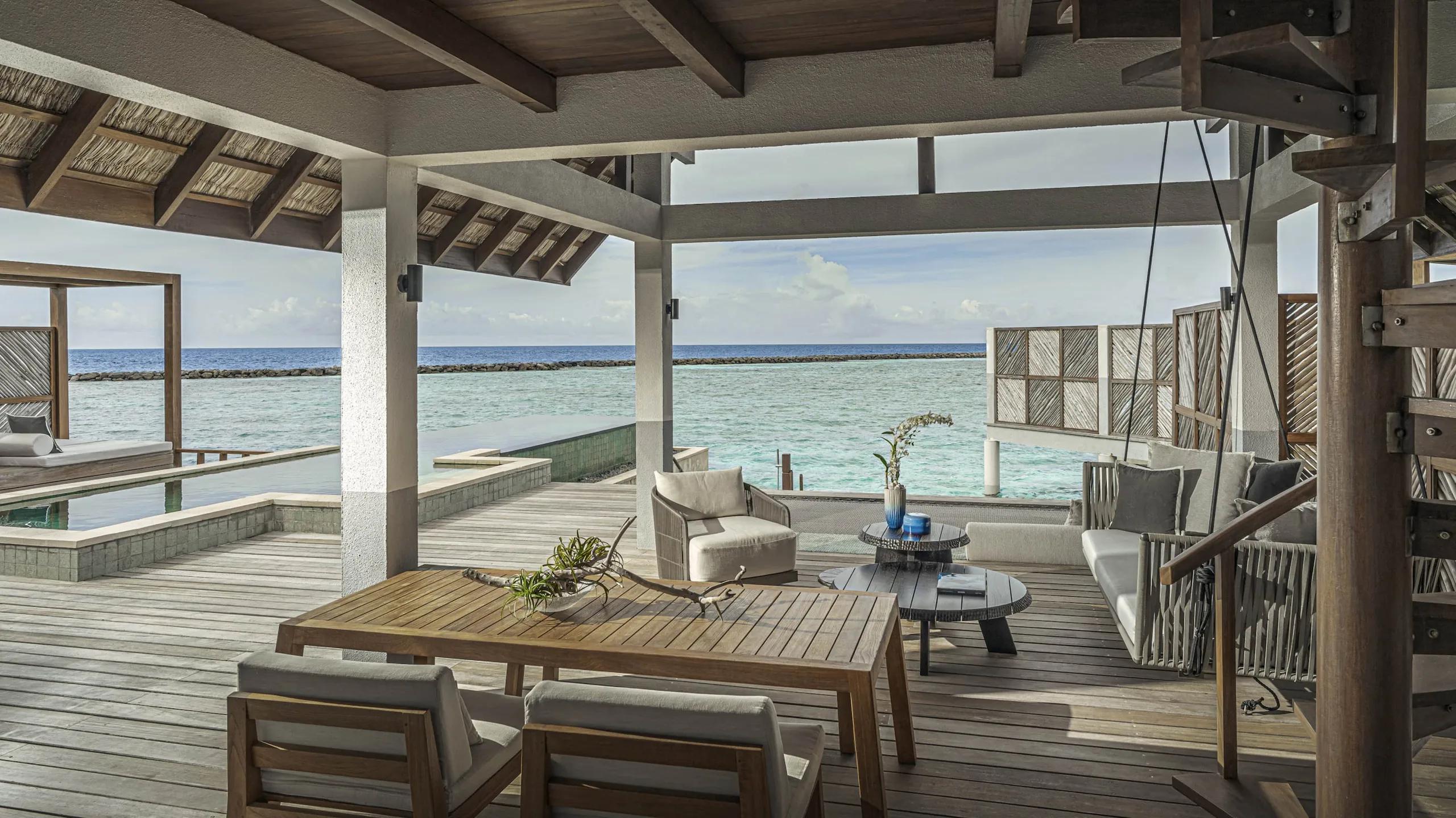 The overwater deck of a Water Villa with Partial Sea View, plunge pool and loungers with the breakwater visible across the lagoon