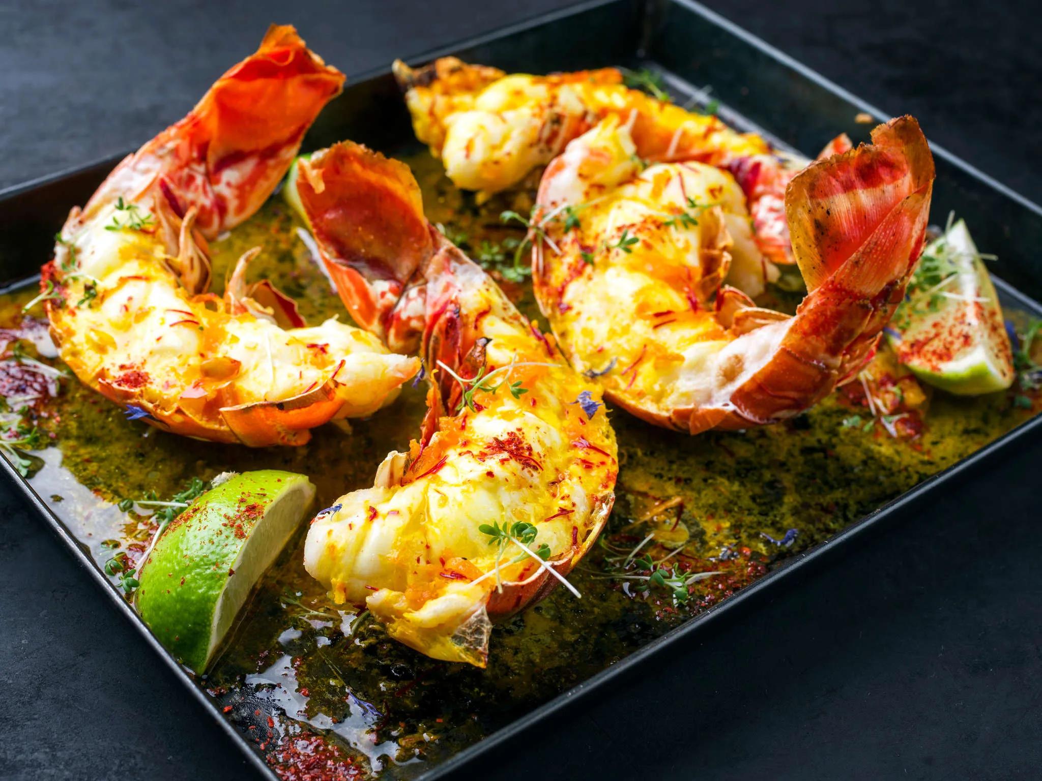 Grilled lobster tails finished with saffron and chilli, plated with lime wedges on a dark tray