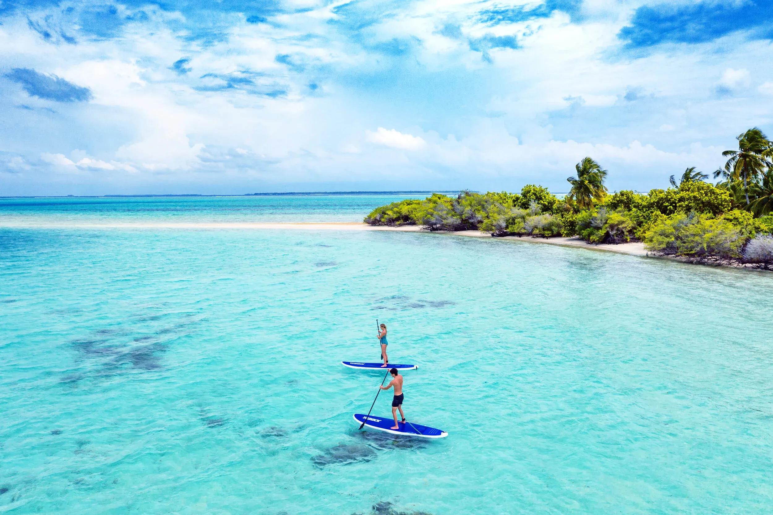 Two guests stand-up paddleboarding toward a small sandy islet near Ayada