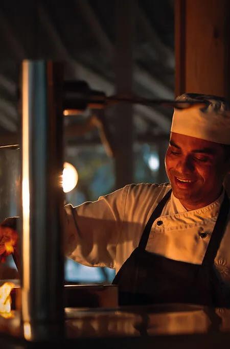 A chef tends the open charcoal grill flame at Carne Diem Grill by Dharshan