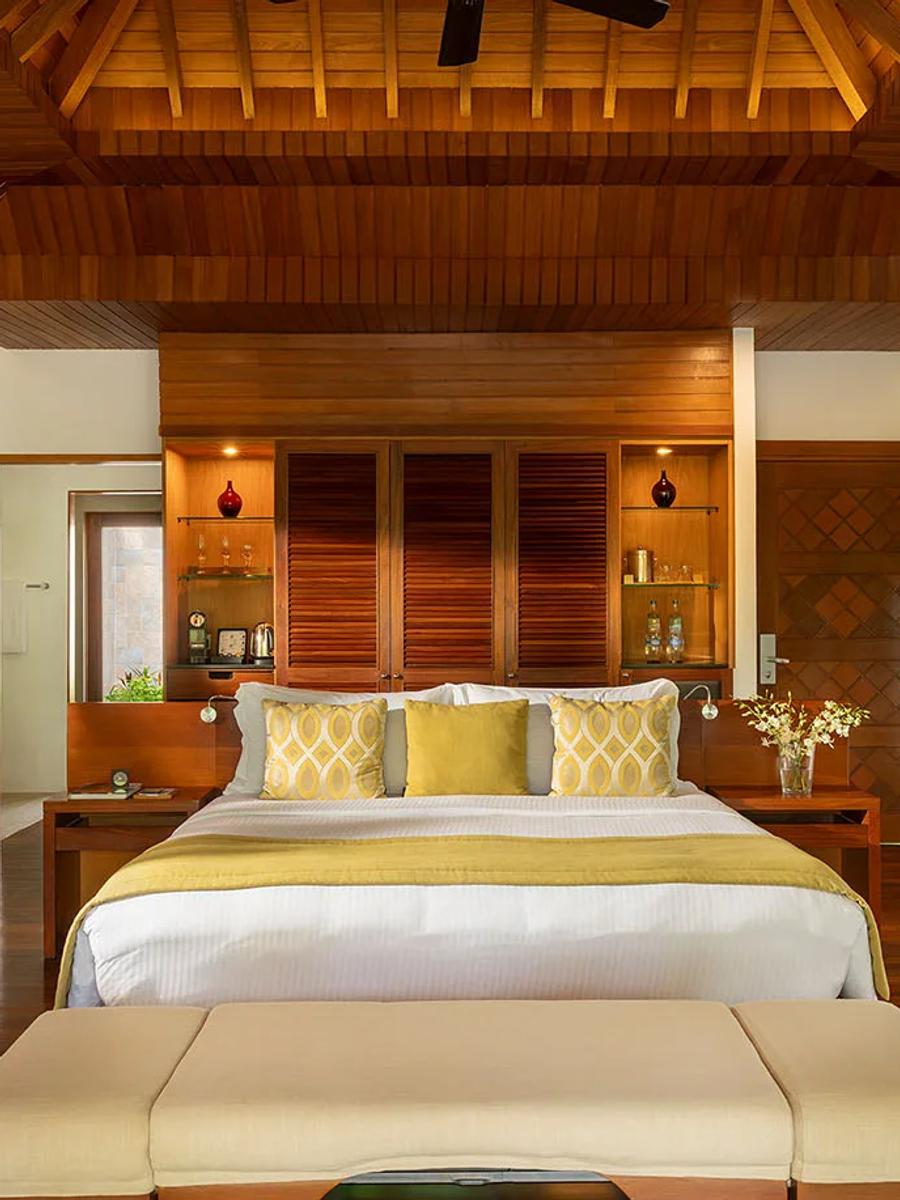 A Baros Villa bedroom with a king-size four-poster bed, dark timber ceiling beams, and doors open to a garden view