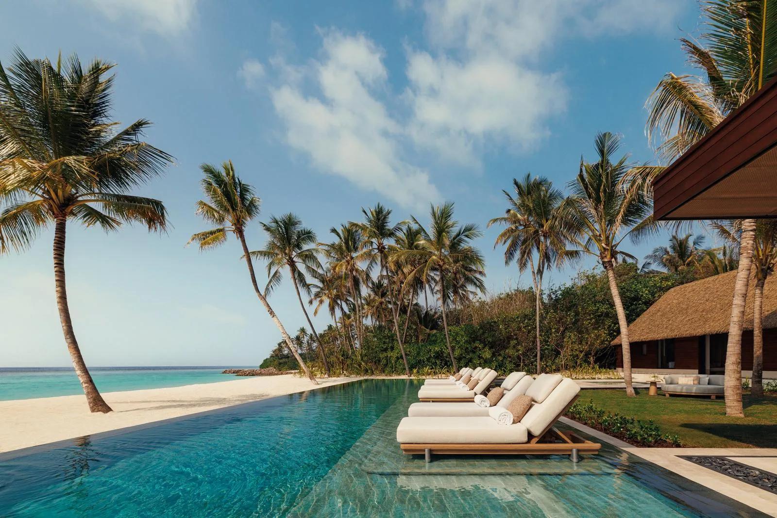An infinity pool and sun loungers on the beach outside a Grand Residence at One&Only Reethi Rah