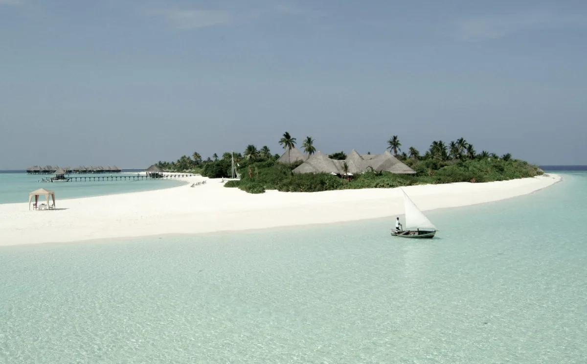 Coco Palm Dhuni Kolhu seen from the lagoon, overwater villas on the jetty and a traditional dhoni under sail in the foreground