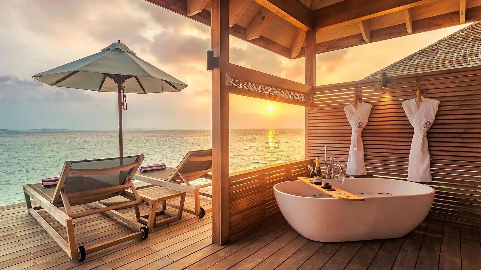 A freestanding bathtub on a Romantic Ocean Villa's open terrace, set for sunset with robes hanging nearby