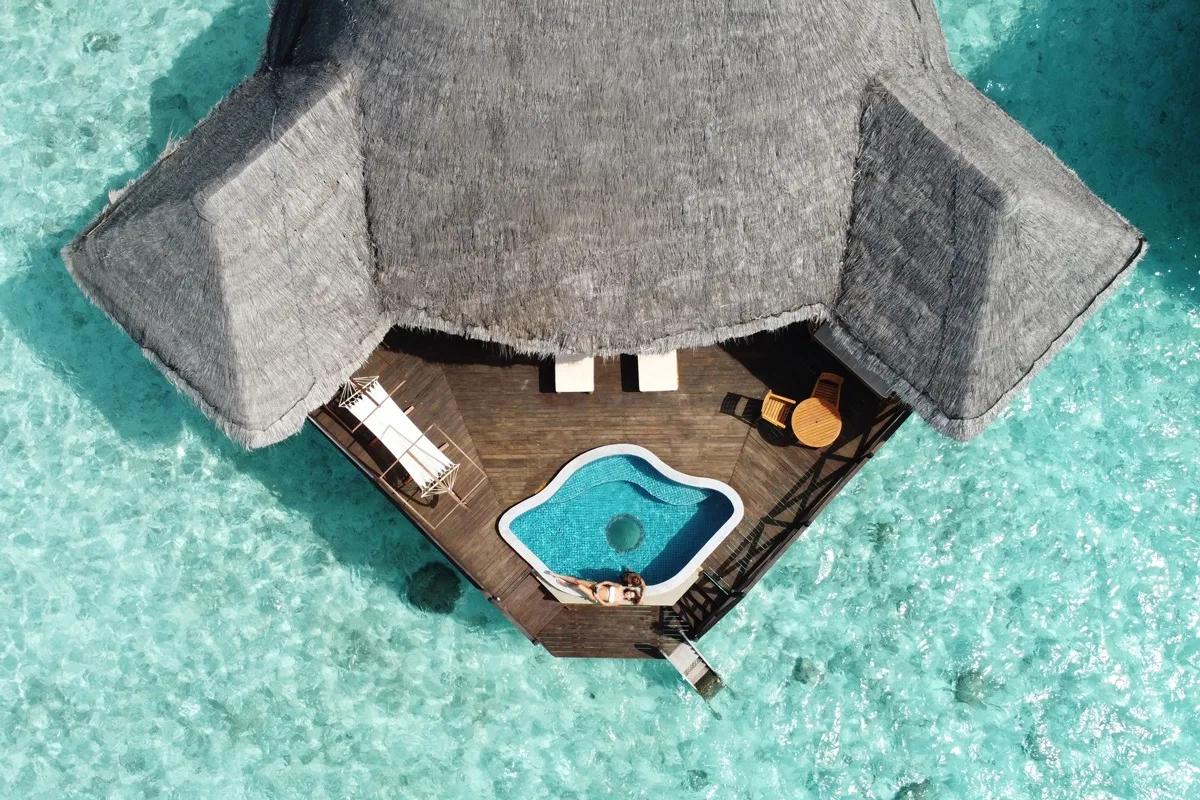 Aerial view directly above an overwater villa's private deck and plunge pool, with a guest swimming