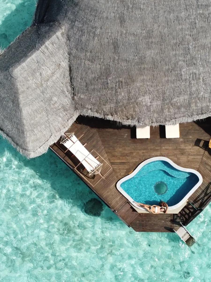 Aerial view directly above an overwater villa's private deck and plunge pool, with a guest swimming