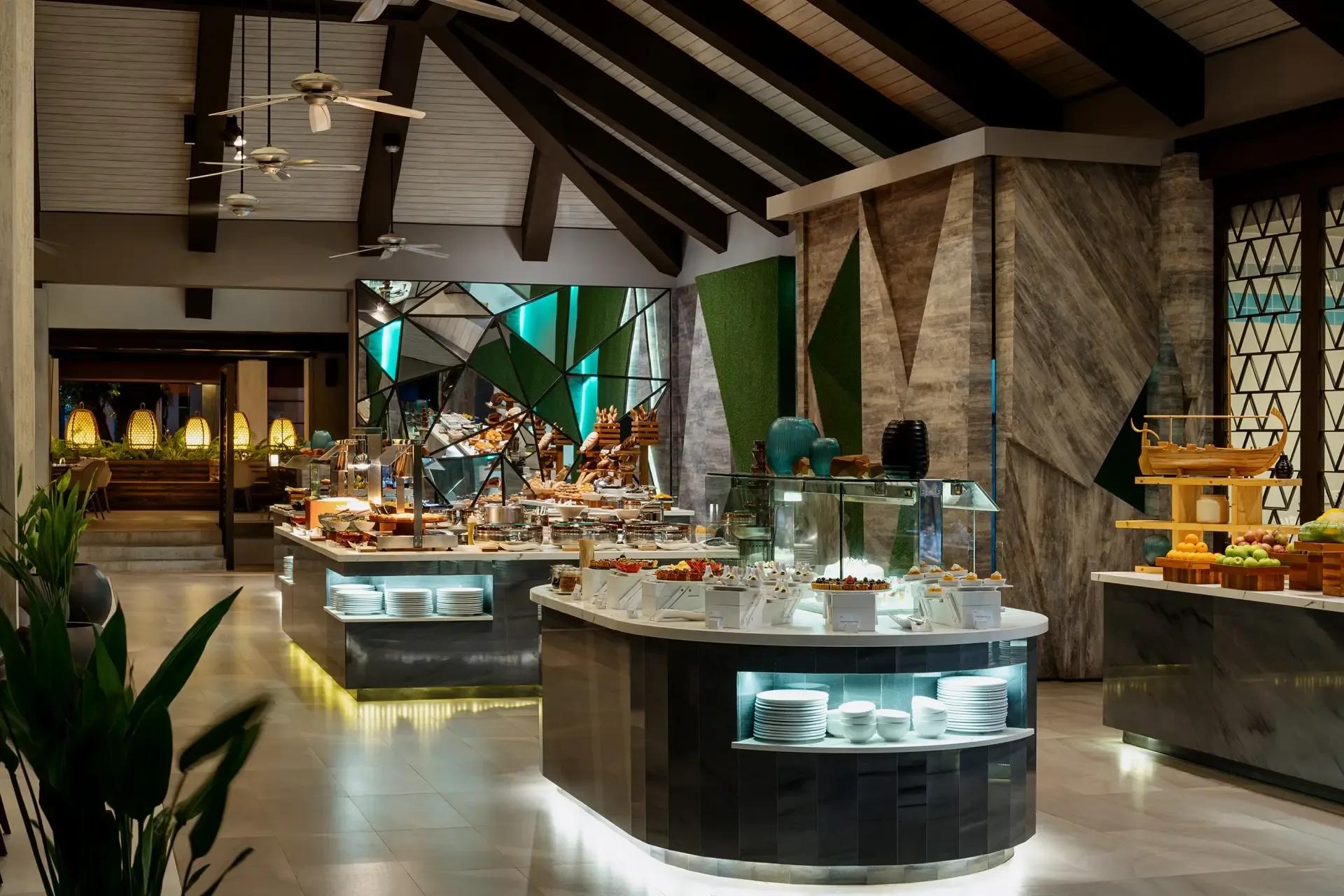 Live cooking stations at Vela laid out with breads, pastries and chafing dishes under a vaulted roof