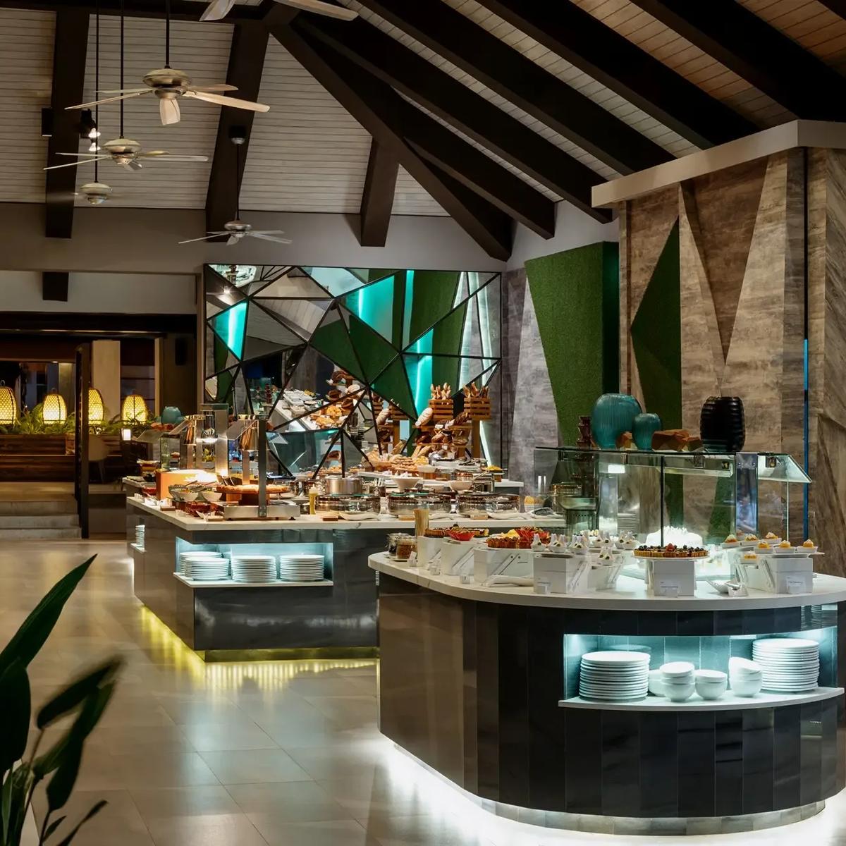 Live cooking stations at Vela laid out with breads, pastries and chafing dishes under a vaulted roof