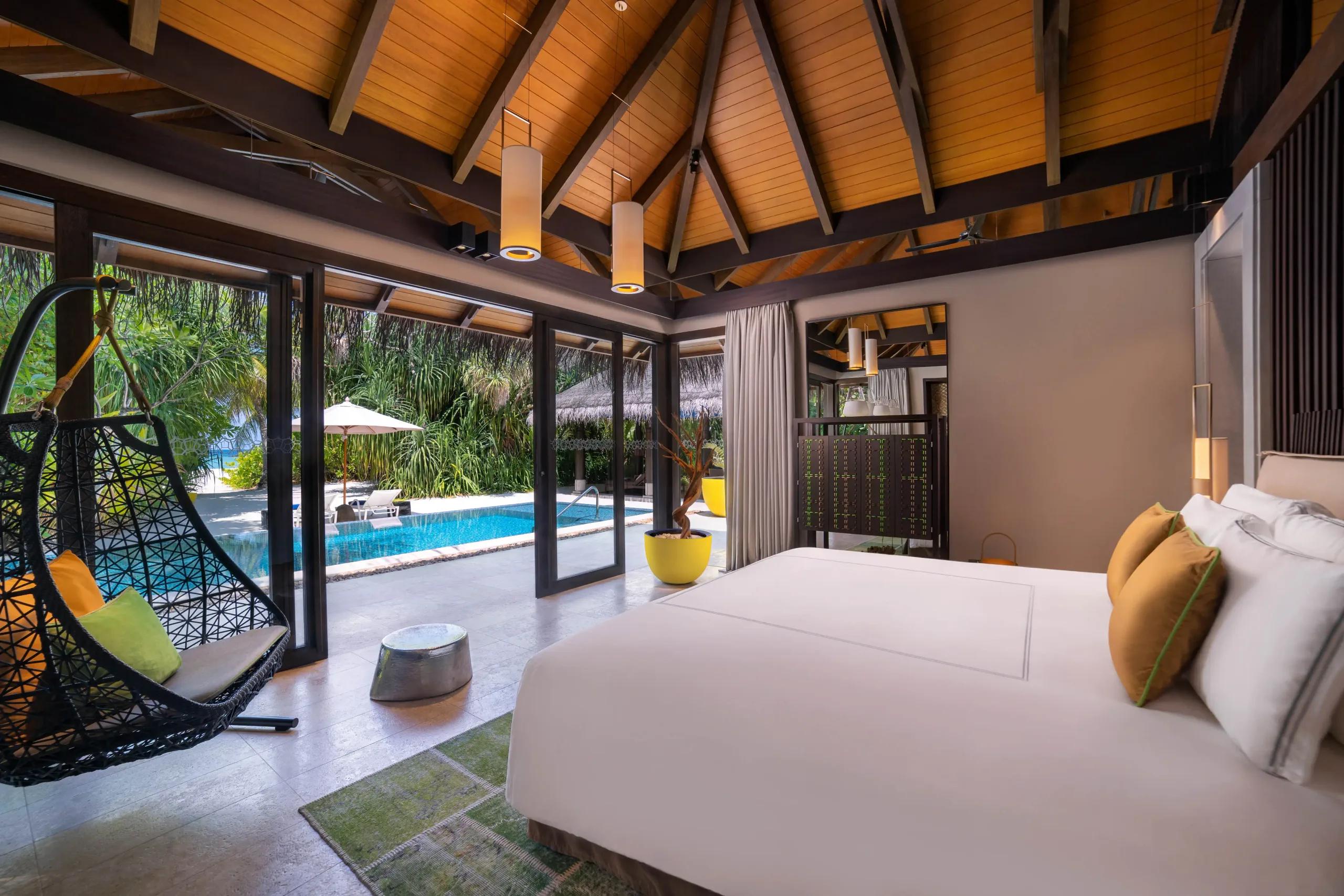 A villa bedroom opens through glass doors onto its own pool and beachfront garden at a Deluxe Beach Pool Villa