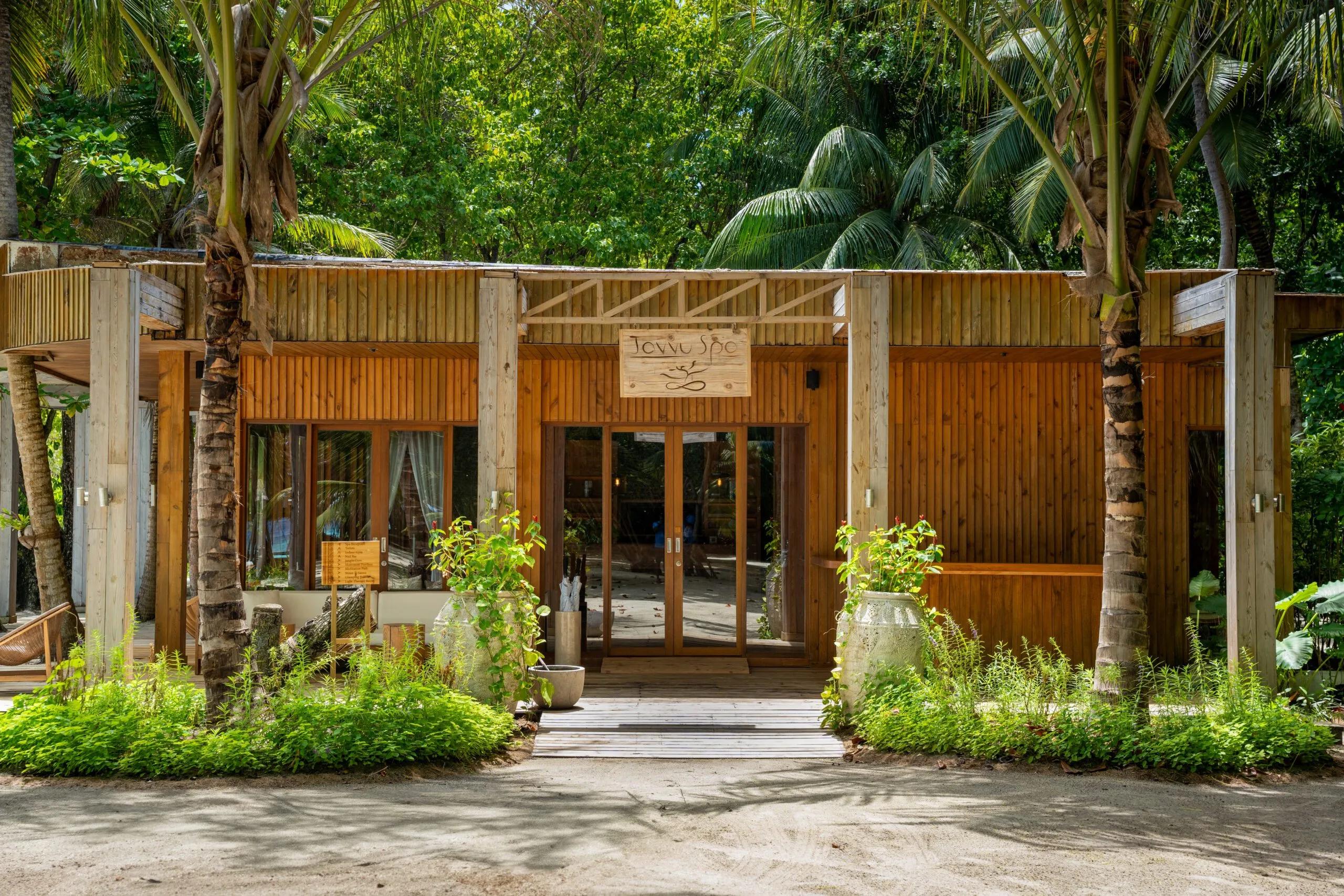 The timber entrance to Javvu Spa at Amilla, palm trees framing its sign and open doorway