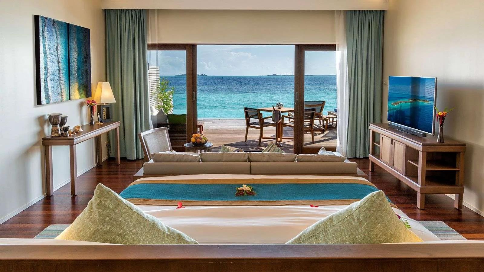 The living area of an Ocean Pool Villa, sliding doors open onto the overwater deck and lagoon beyond