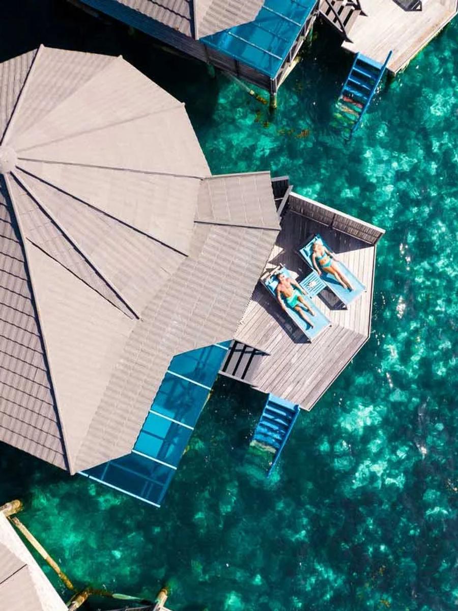 Bird's-eye view of an overwater villa deck at Kuredu, guests sunbathing above clear lagoon water