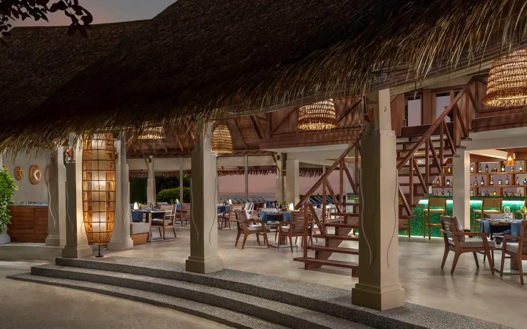 Aqua's open-air dining room under a thatch roof, with rattan lampshades and wooden-framed chairs