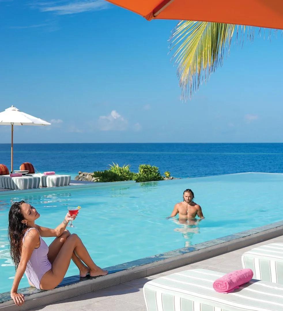 A couple at the infinity pool of West Beach Bar, OBLU SELECT Lobigili, the pool edge blending into the open ocean