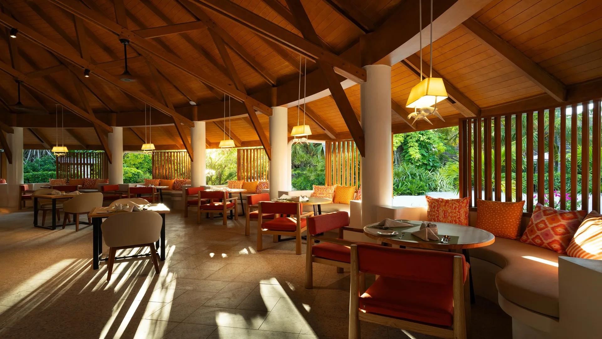 The interior of Gallery restaurant at Bandos, wooden dining tables set beneath a high wood-raftered roof open to the garden