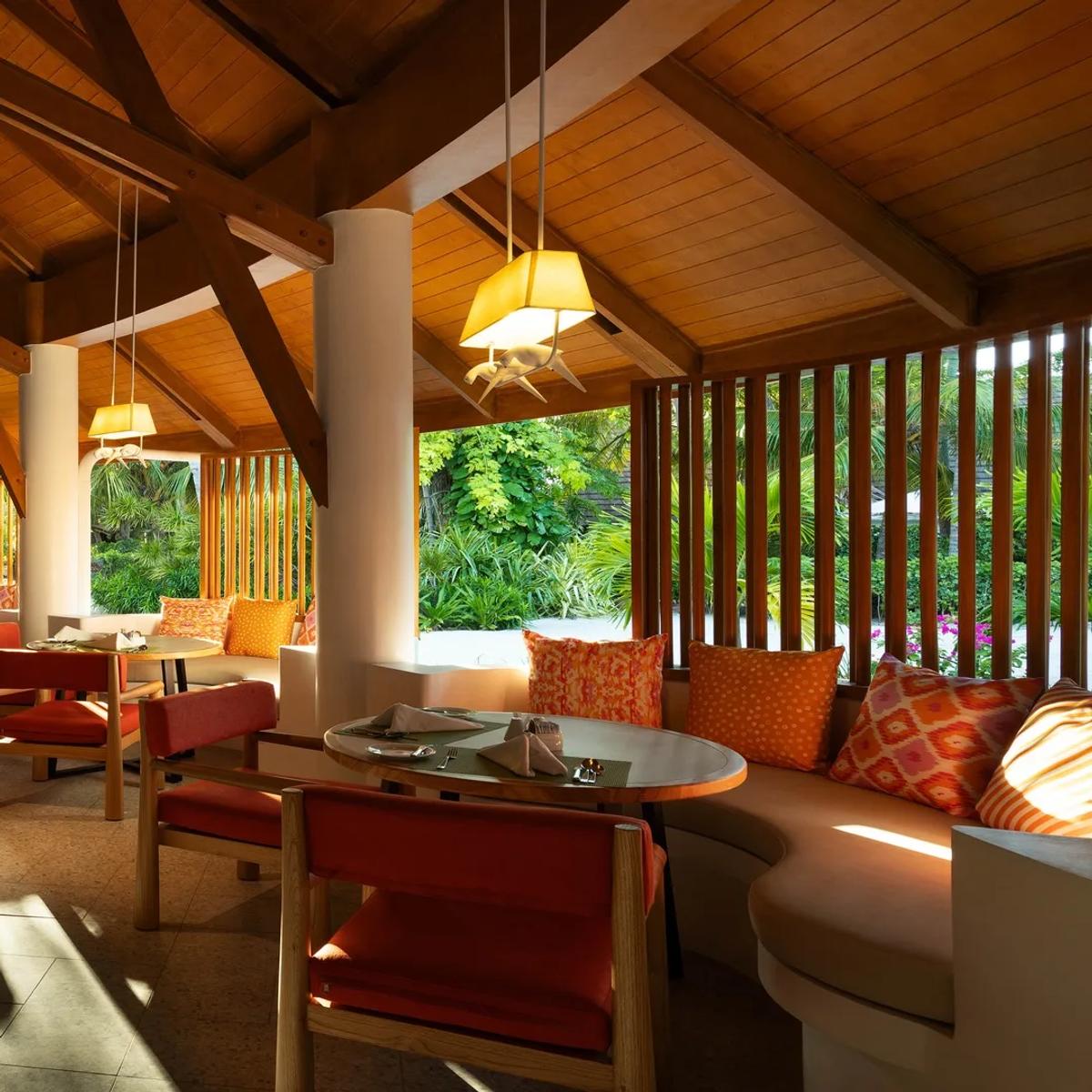 The interior of Gallery restaurant at Bandos, wooden dining tables set beneath a high wood-raftered roof open to the garden